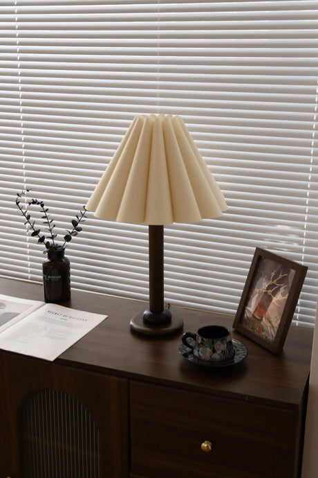 Pleated table lamp seen across a room on a dark wood dresser