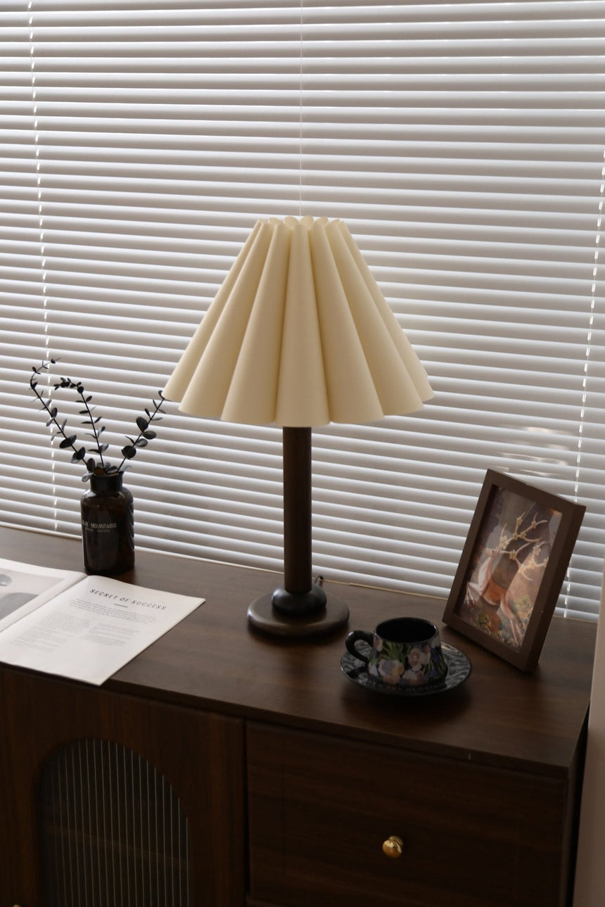 Pleated table lamp seen across a room on a dark wood dresser