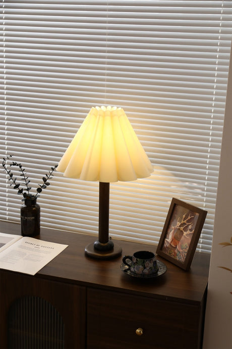 Pleated table lamp lit and seen at an angle on a dark dresser