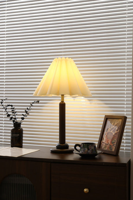 Pleated table lamp lit close, the linen cone and wood column in view