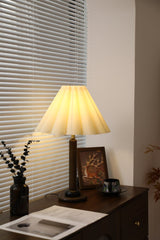 Pleated table lamp lit in a corner beside a framed picture