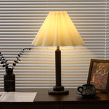 Pleated table lamp lit warm, the pleats glowing along each fold