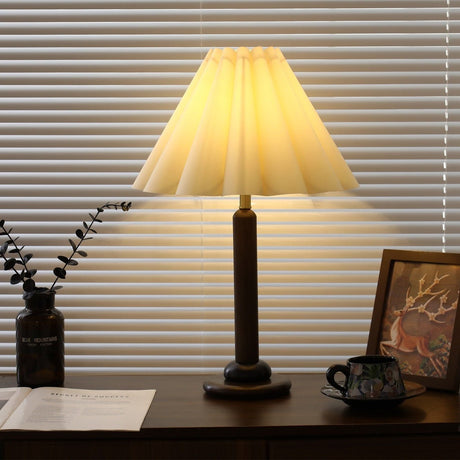 Pleated table lamp lit warm, the pleats glowing along each fold