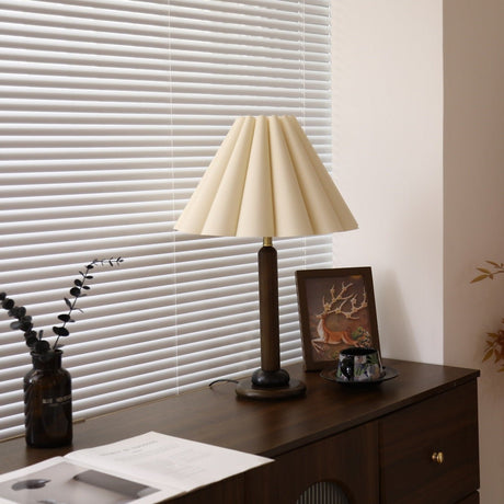 Pleated table lamp lit on a dark dresser beside a framed picture