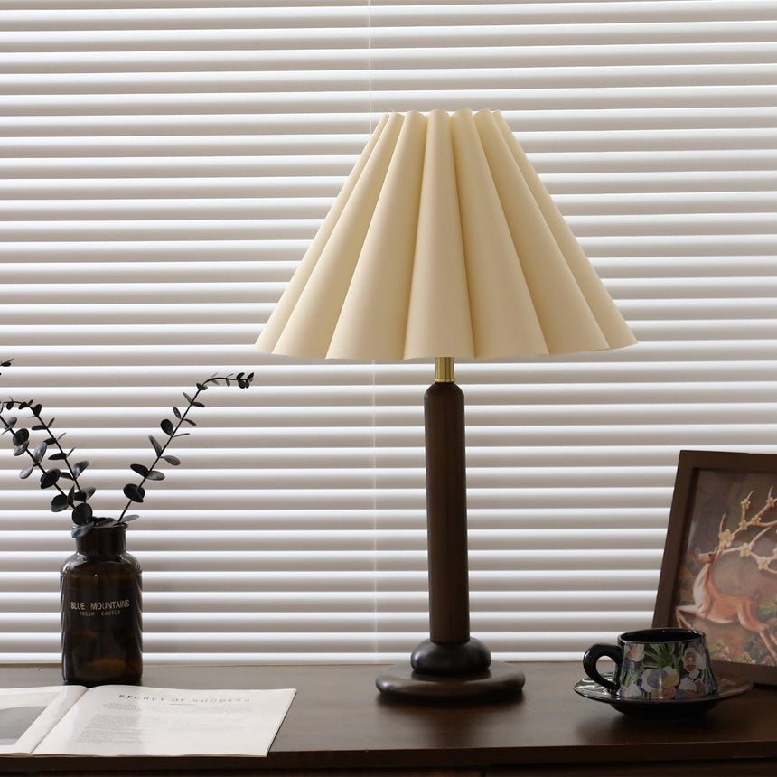 Pleated table lamp seen three quarters on beside a framed picture