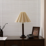 Pleated table lamp unlit on a dresser in front of window blinds