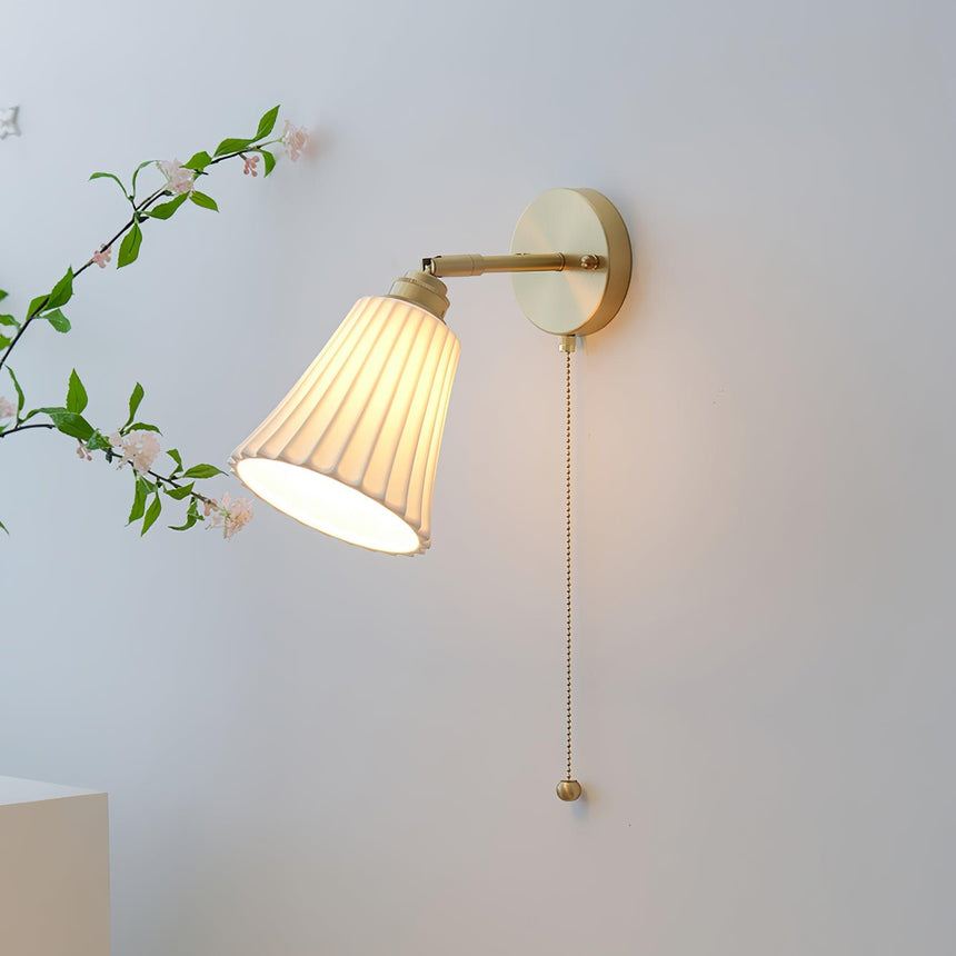 The pleated shade lit on a pale wall beside a flowering branch