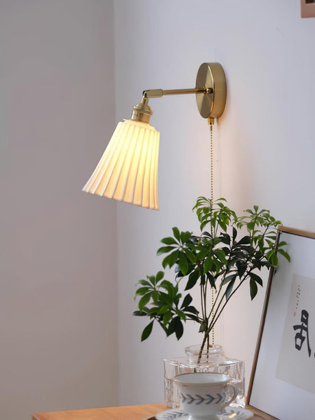 The sconce lit above a wood cabinet with a plant in a glass vase