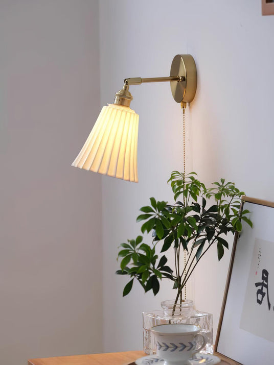 The sconce lit above a wood cabinet with a plant in a glass vase