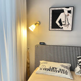 The sconce lit on a wall above a houndstooth headboard and a framed print