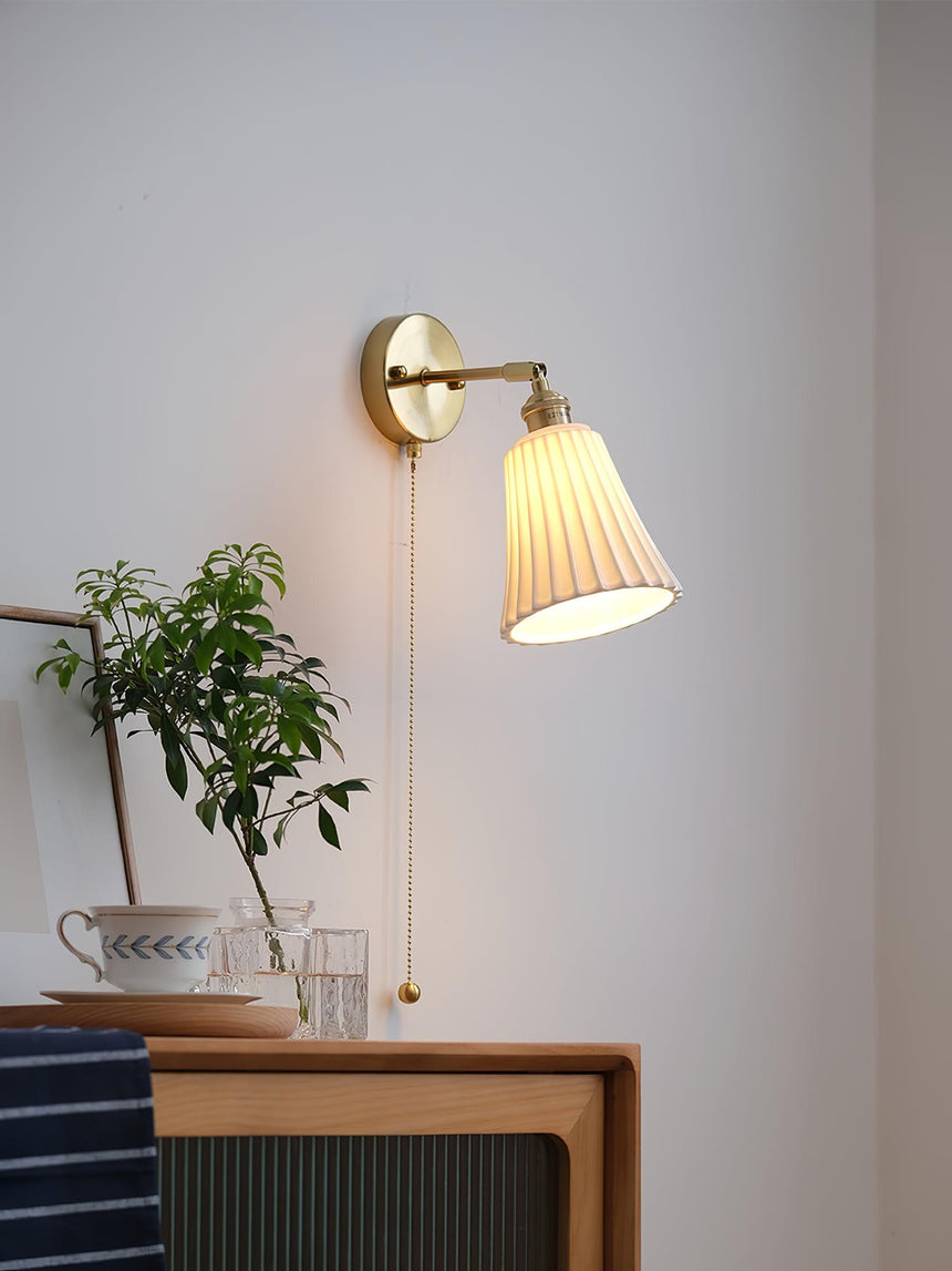The small sconce above a wood nightstand with a plant and a cup