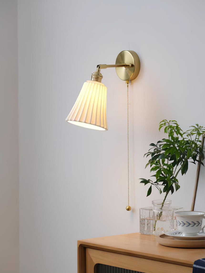 The sconce lit above a cabinet, its pull chain hanging beside a plant