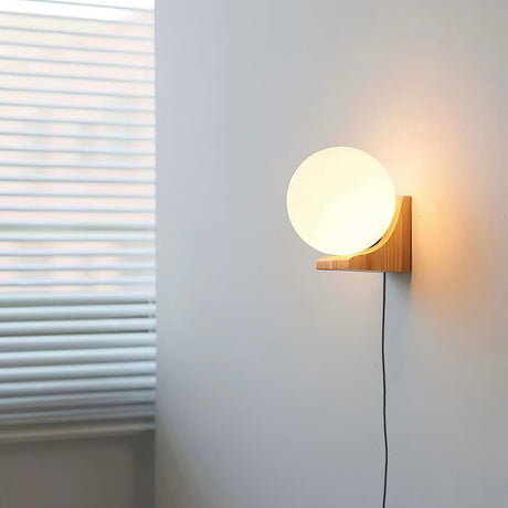 Glass orb sconce lit on a wall beside a window with slatted blinds