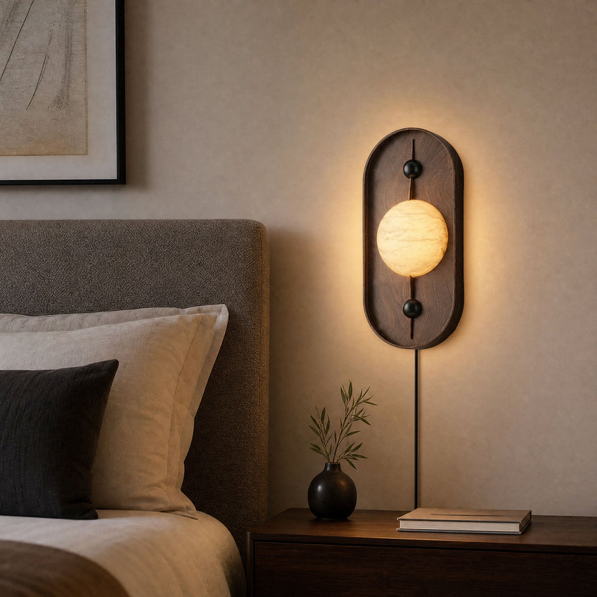 Lamp lit beside a headboard above a nightstand with a small stone vase