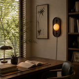 Lamp lit above a wood desk with an open book beside a bright window