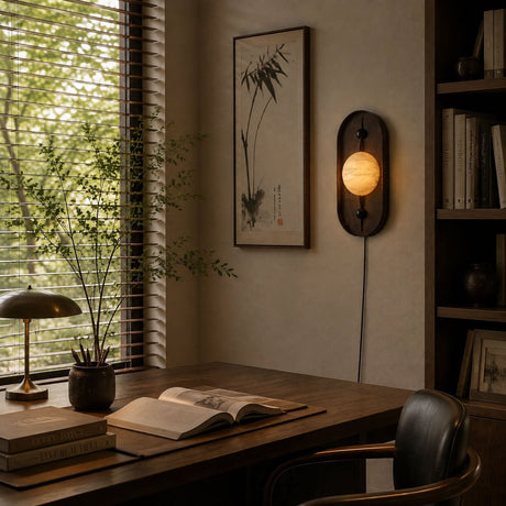 Lamp lit above a wood desk with an open book beside a bright window
