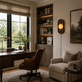 Lamp lit in a study beside a desk, a bookcase and a tall window