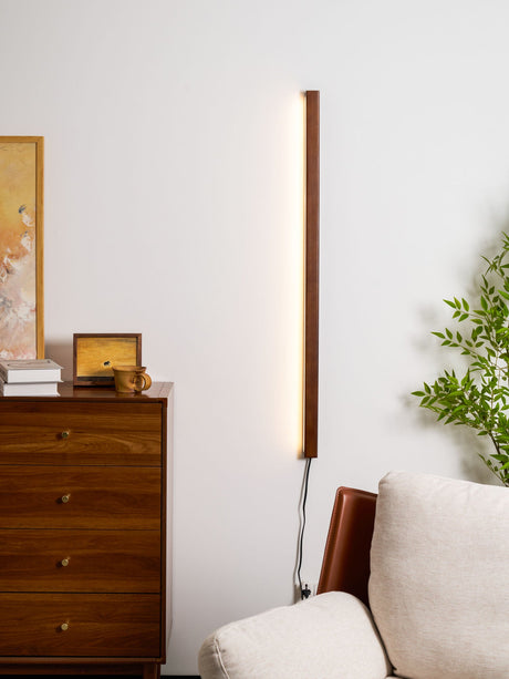 Walnut bar lit vertically beside a chest of drawers and an armchair