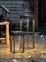 The lantern lit on paving beside a bamboo screen and a brick wall