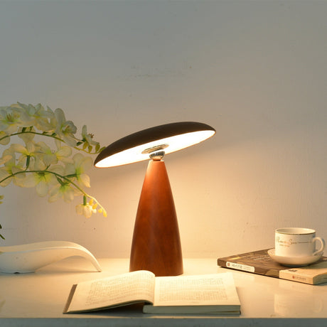 Portable table lamp lit warm on a desk beside a cup