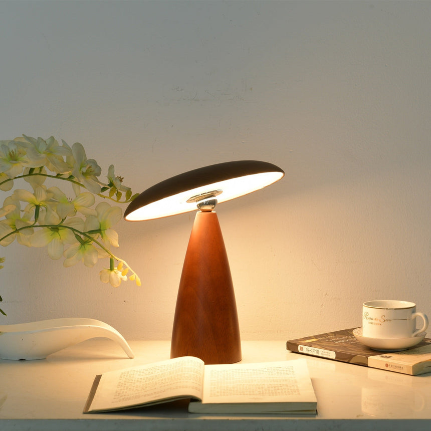 Portable table lamp lit warm on a desk beside a cup