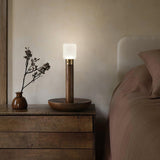 Portable table lamp lit on a wood dresser beside a small vase of twigs
