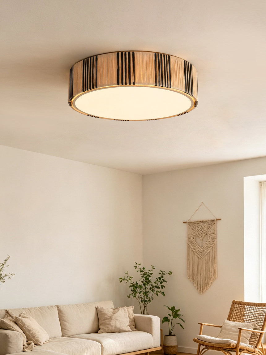 Striped raffia drum ceiling light in a living room with a corner sofa and a wall hanging