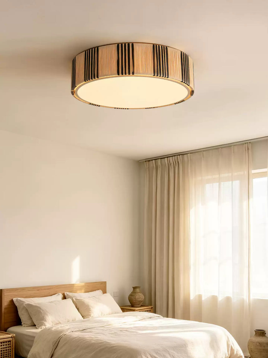 Striped raffia drum ceiling light above a bed beside a curtained window