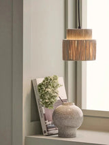 Rattan drum pendant light lit in an interior with a vase
