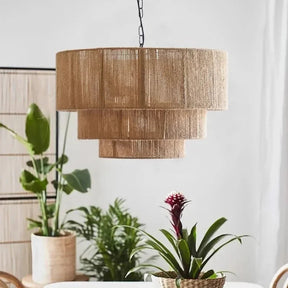 Rattan drum pendant light with three fringed tiers lit above a row of plants