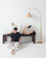 Brass arc beside a dark bench, two people reading under the woven shade