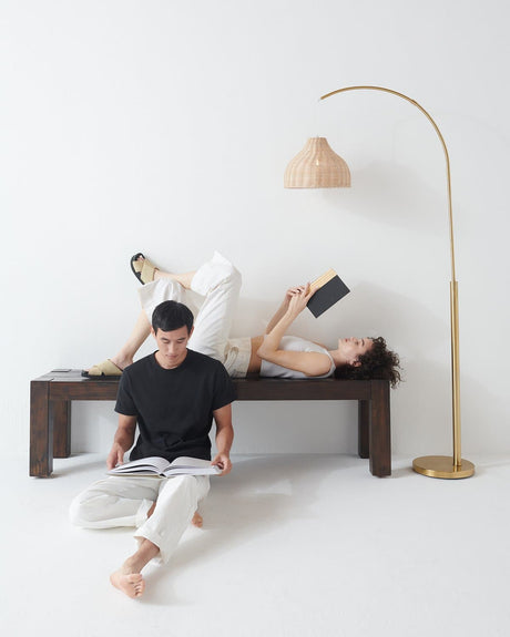 Brass arc beside a dark bench, two people reading under the woven shade