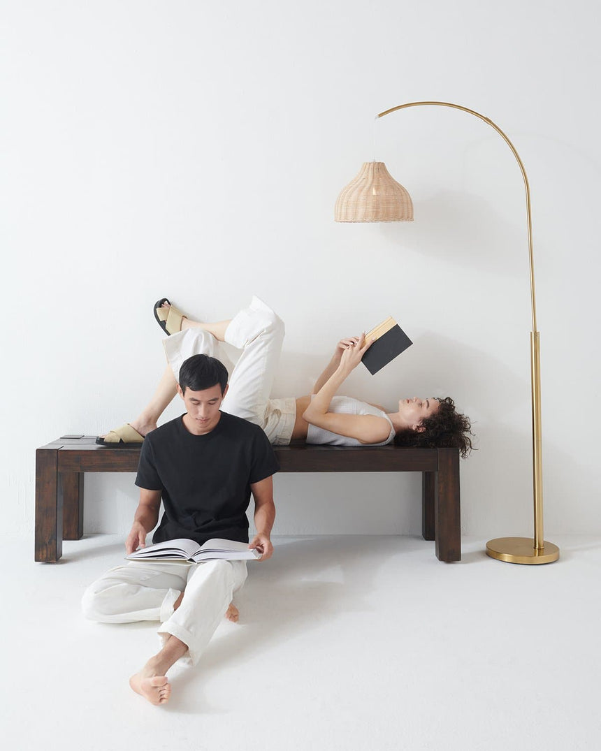 Brass arc beside a dark bench, two people reading under the woven shade