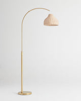 Brass arc floor lamp with a woven wicker shade hung from the end of the curve