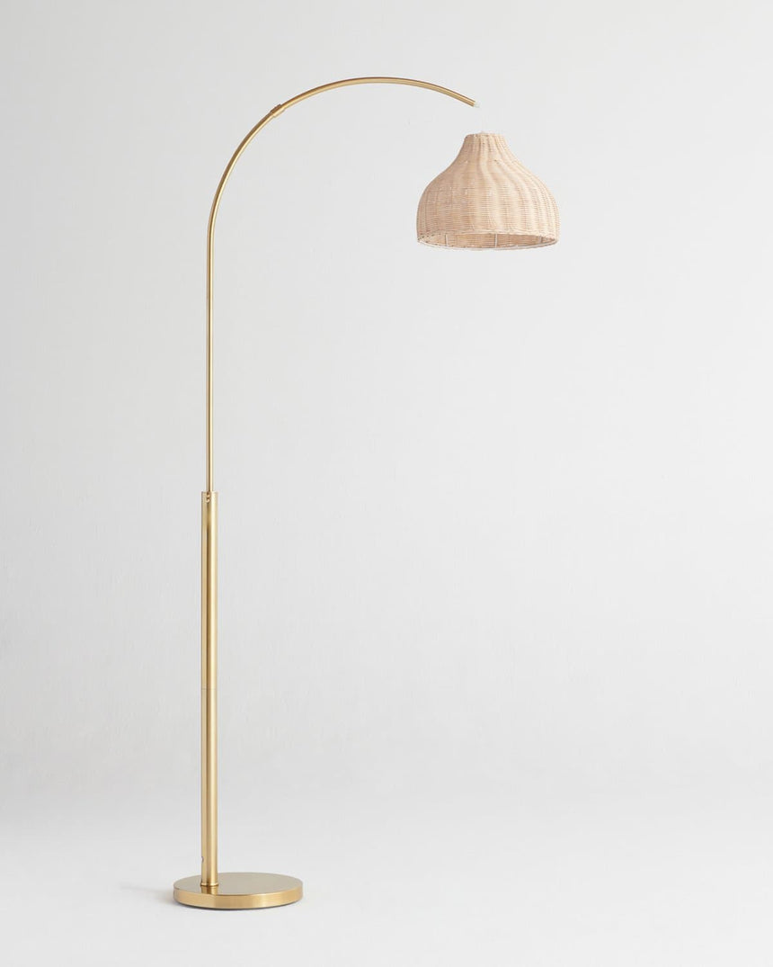 Brass arc floor lamp with a woven wicker shade hung from the end of the curve