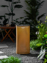 The lantern glowing on a gravel border beside grasses and a stepping stone