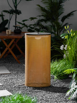 The lantern lit on gravel beside ornamental grasses and a paving slab