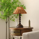 Rattan shade lamp lit beside a tall green plant and a candlestick
