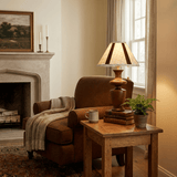 Table lamp lit on a side table beside a leather armchair and a fireplace
