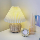 Rattan table lamp lit in a corner beside a candle and a photo frame