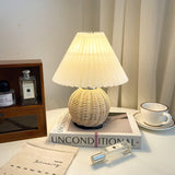 Rattan table lamp lit on a dressing table beside a cup and magazines