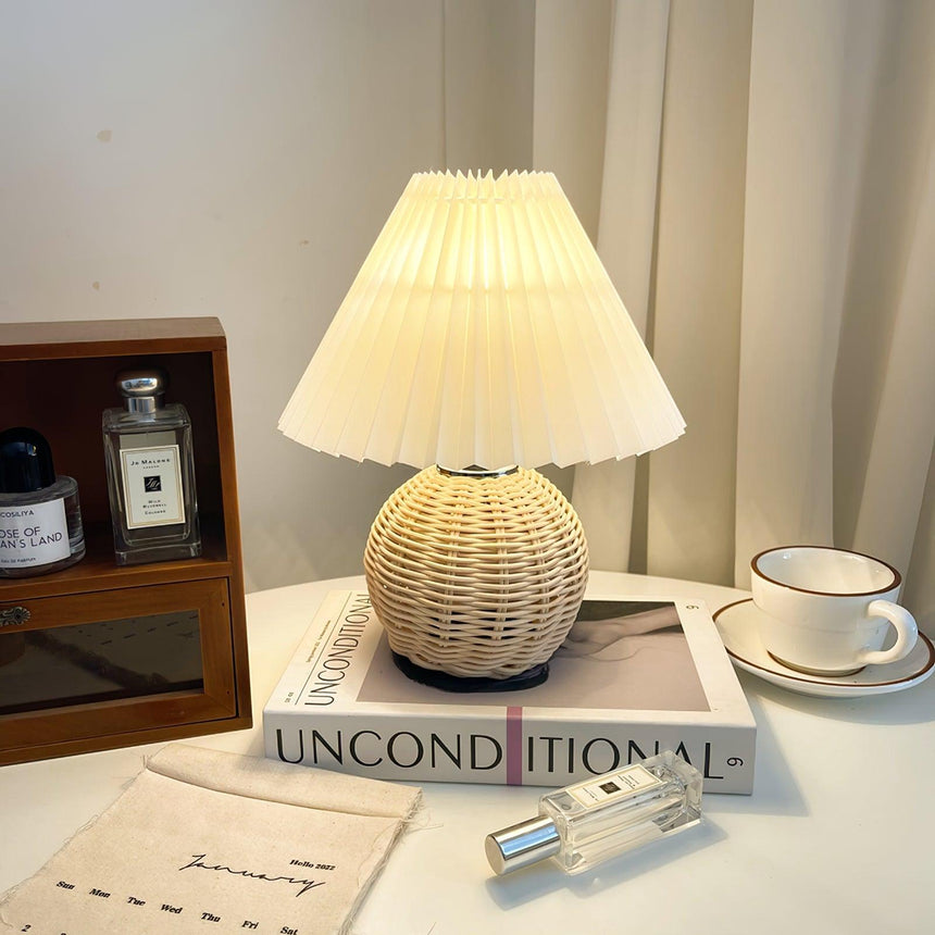 Rattan table lamp lit on a dressing table beside a cup and magazines