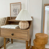 Rattan table lamp on a wooden nightstand beside a mirror