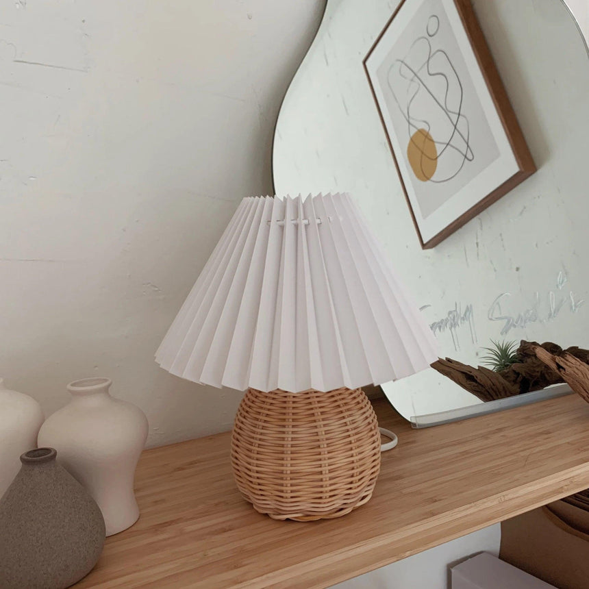 Rattan table lamp on a wooden shelf below a framed print