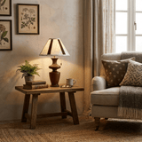 Plaid shade table lamp lit on a wooden bench beside a gray sofa