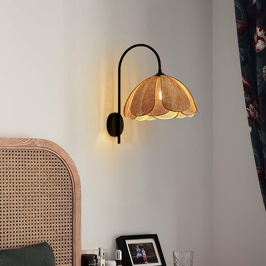 The rattan sconce lit above a cane headboard and a framed photo on a nightstand