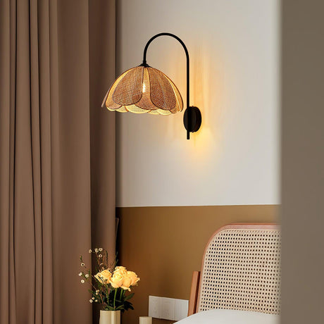 The rattan sconce lit beside a brown curtain above a cane chair and flowers
