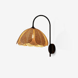Wall sconce with a black gooseneck arm and a woven rattan shade shaped like petals