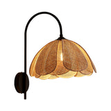 The sconce in profile, the black arm curving over to hold the rattan shade