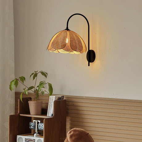The rattan sconce lit above a low wood shelf with a plant and books